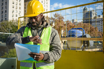 young black engineer man with helmet and vest outdoors watching the time to go to eat and rest.