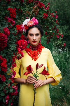 Brunette woman in a yellow dress with red jewelry in red roses 