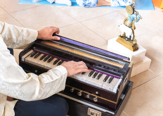 hands of an unrecognizable buddhist musician with his back turned playing a harmonium next to a murlidhar image