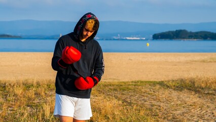 young boxer putting on his boxing gloves with a sea view