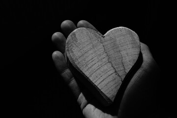 Männliche Hand mit einem Herzen aus Holz als Symbol von Trauer.