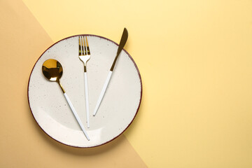 Clean plate with set of golden cutlery on beige background, closeup