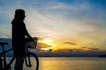 girl watching the horizon with a bike on a beautiful sunset on the sea