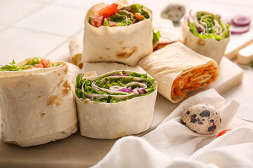 Board of tasty lavash rolls with vegetables on white tile background