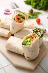 Board of tasty lavash rolls with vegetables on white tile background