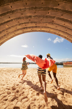 Young friends running through tunnel into water on harbor beach while on summer holiday 