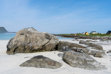 de gros rochers sur une plage de sable blanc et des  maisons en fond sous un ciel bleu - 622062155
