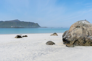 un décors avec un gros rocher sur une plage de sable blanc et une eau  bleu claire