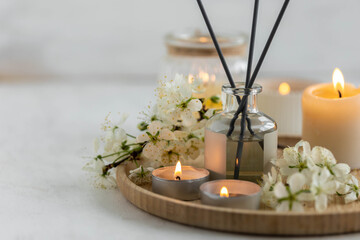 Fototapeta na wymiar Cozy home decor, hygge and aromatherapy concept. Comfortable atmosphere, spring delicious fresh smell. Aroma diffuser, burning candle, cherry blooming flowers and perfume on wooden bamboo tray.
