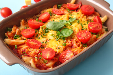 Baking dish of pasta with tomato sauce and cheese on blue background