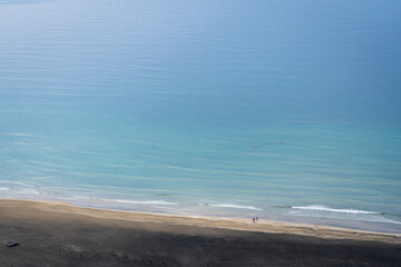 une plage d'un bleu intense et de sable blanc avec une  personne qui se promène