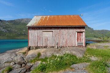 la façade d'une cabane en bois à la peinture écaillée au bord d'un lac bleu et de montagnes