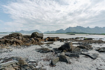 des rochers sur une plage sous un ciel laiteux et des montagnes en arrière plan