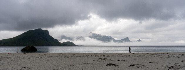 panorama sur une plage du nord avec une personne en silhouette, des nuages et des montagnes  - 622063999