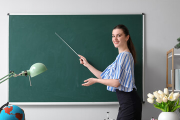 Female teacher with pointer near chalkboard in classroom