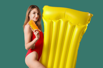 Obraz premium Young woman with sunscreen cream and inflatable mattress on green background