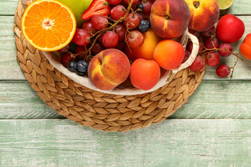 Wicker basket with different fresh fruits on green wooden background