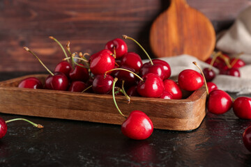 Wooden board sweet cherries on black table