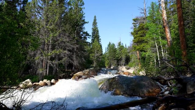 a powerful rushing river from snow melt flows in the mountains with sound audio of the water streaming by and blue skies above