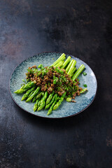 Green asparagus glazed with minced meet and herbs served as close-up on a design plate with text space