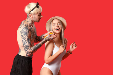 Young couple with sunscreen cream on red background