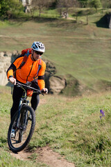 Young man cycling on a rural road through green spring meadow during sunset