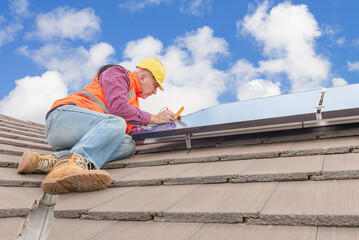 experienced worker checking solar panels on house roof