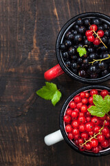 Fresh delicious organic red and black currants in a mugs on wooden table