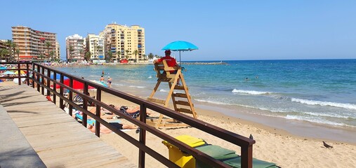 A lifeguard watches over vacationers at sea. Lifeguard on the tower on the beach under an umbrella....