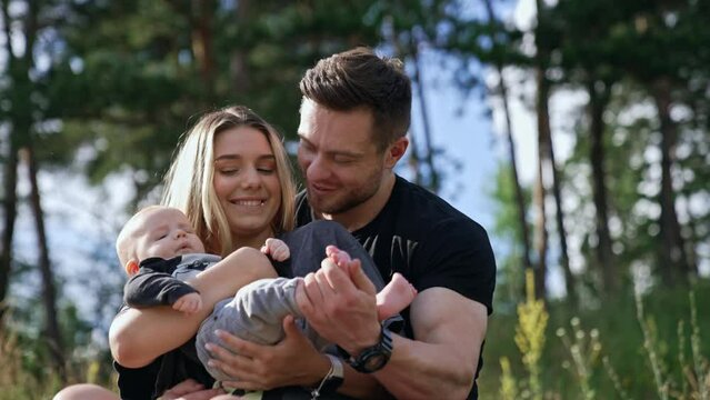 Caucasian family with a tiny baby resting in the sun. Happy people adoring their newborn kid rest in nature.
