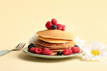 Plate of tasty pancakes with raspberries and blueberries on yellow background