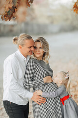 portrait of a young pregnant woman with her family outside in a park among yellowed leaves