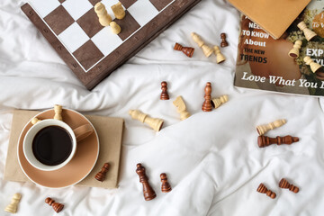 Chess pieces with cup of coffee and magazine on bed, top view