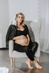 stylish studio portrait of a beautiful pregnant young woman on a chair in a black suit