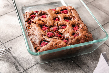 Baking dish with raspberry chocolate brownie on grey tile table
