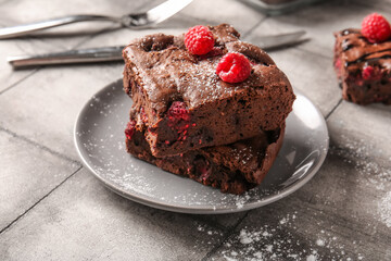 Plate with pieces of raspberry chocolate brownie on grey tile table