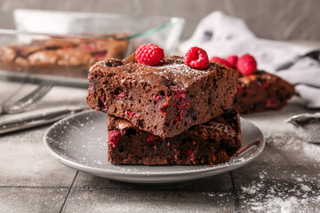 Plate with pieces of raspberry chocolate brownie on grey tile table