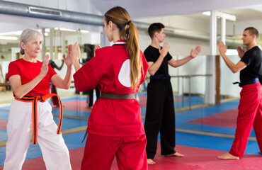 Fototapeta premium Portrait of concentrated senior woman wearing traditional sportswear sparring with young female opponent during martial arts training in gym