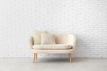 Cozy white sofa with pillows near brick wall