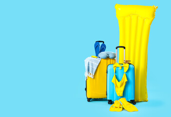 Obraz premium Suitcases with inflatable mattress and different beach accessories on blue background. Travel concept