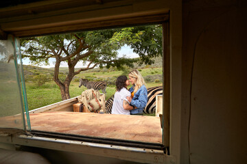 Young queer couple embracing while on safari picnic through vehicle window © Faces of Travel