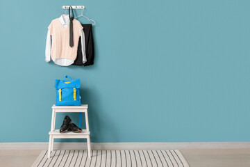 Step ladder with school backpack, shoes and uniform hanging on color wall