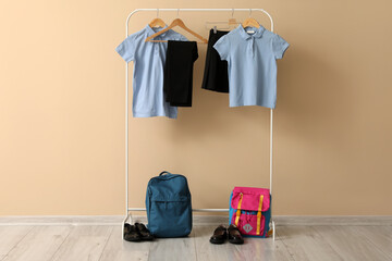 Rack with stylish school uniform, backpacks and shoes near color wall