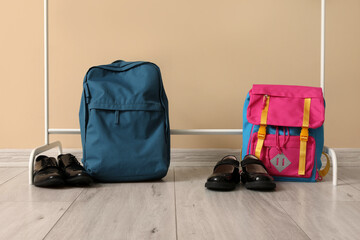 Stylish school backpacks and shoes on floor near color wall