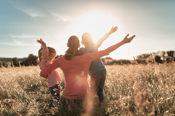 Joyful family morning in the countryside, mother and children raise arms in a field with feelings...