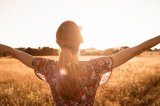 Young woman embraces nature's beauty in a rural, backlit field at sunset.