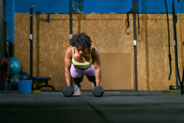 Black sportswoman doing plank exercise with dumbbells