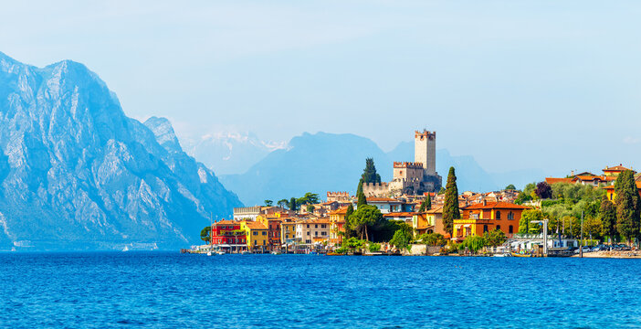 Ancient tower and fortress in old town Malcesine at Garda lake, Veneto region, Italy. High snowbound top mountains on background. Summer landscape with colorful houses and green trees.
