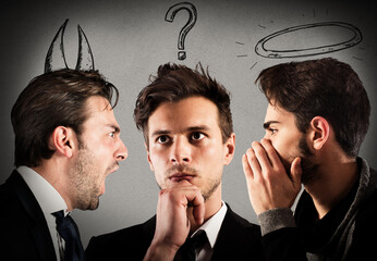 Businessman with thoughtful expression between an angel and a devil