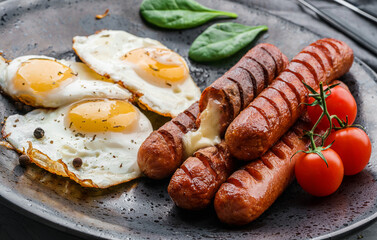 Delicious breakfast with fried eggs, grilled sausages with cheese, tomatoes, greens and spices on plate on dark background. Meat food, selective focus